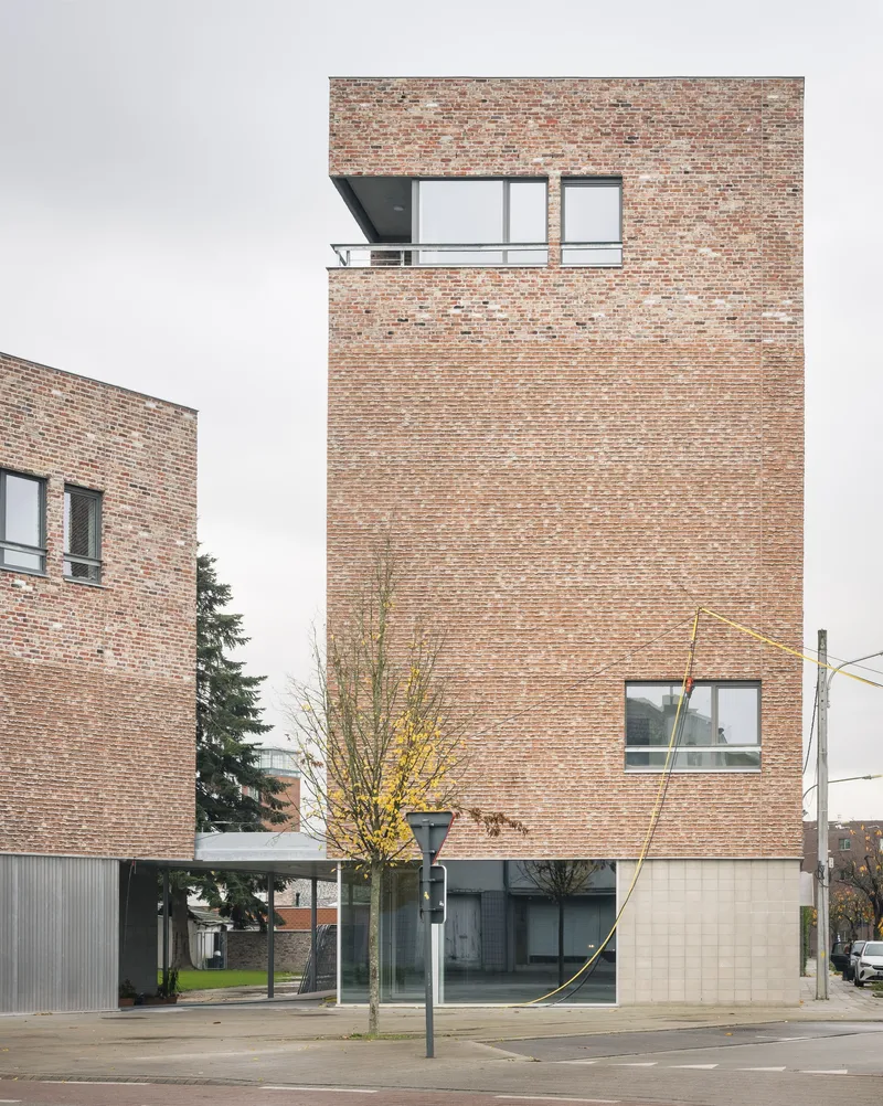 Street view of the brick facade with corner windows and a ground floor carport on an overcast day