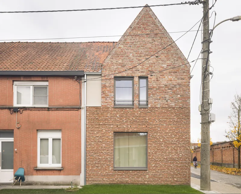 Brick gable facade with varied bond patterns flanked by overhead power lines and neighboring houses