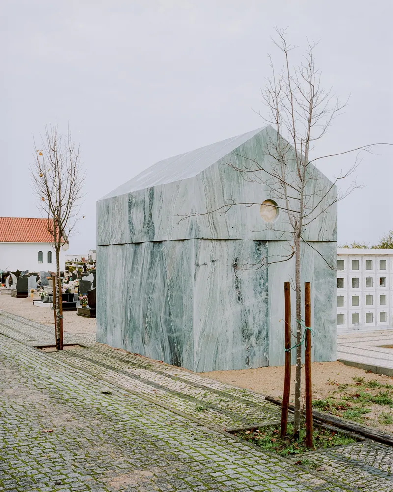 Front facade with circular window and bare trees flanking the marble-clad structure on cobbled ground