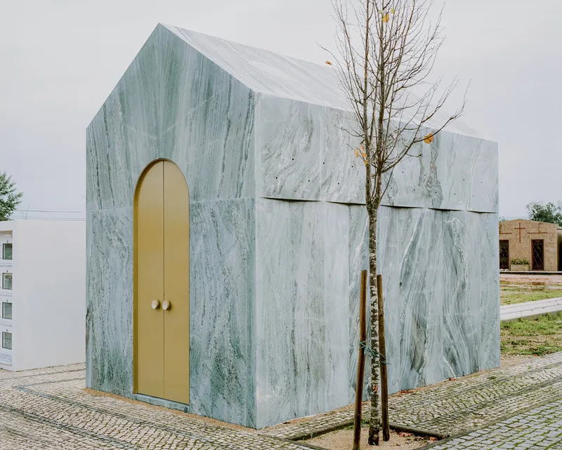 Corner view showing arched brass doorway and veined marble cladding with a young tree alongside