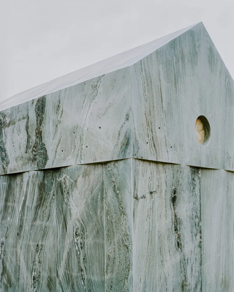 Detail of the upper corner where marble panels meet at the gable edge with circular oculus