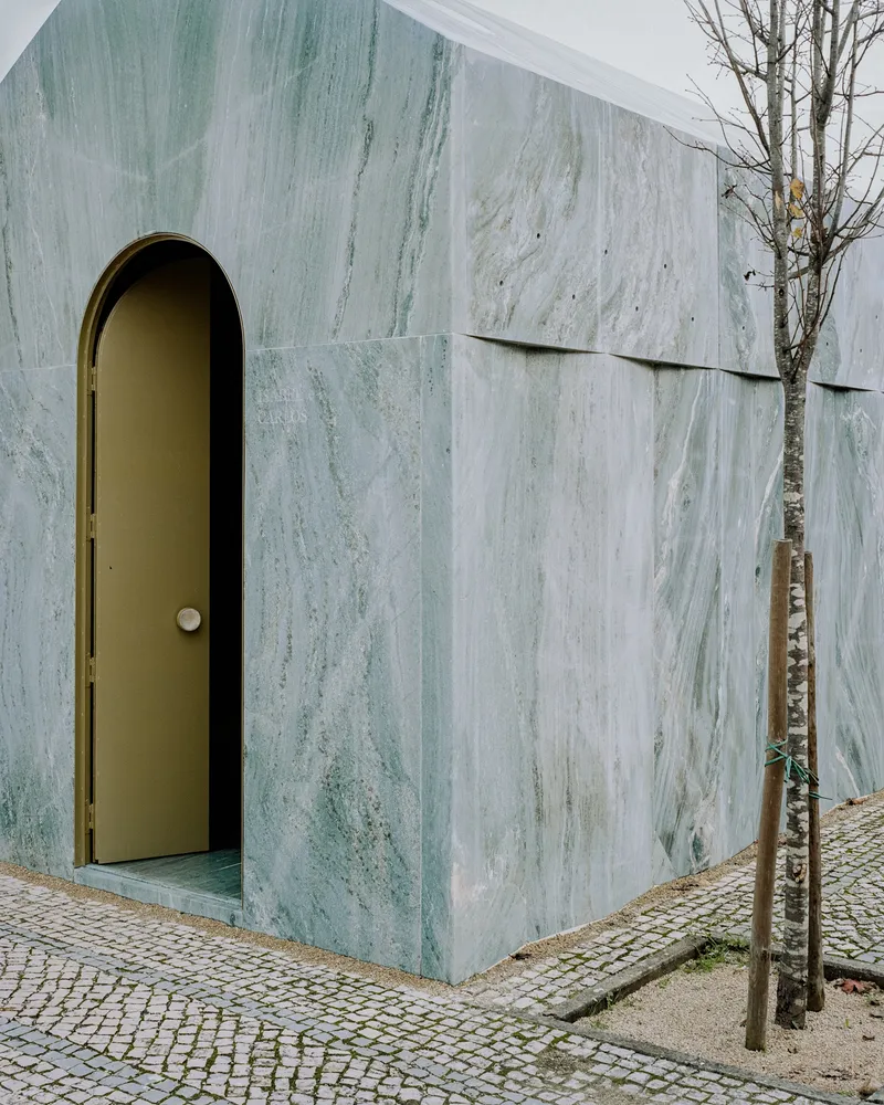 Corner detail of the veined marble facade with arched brass door and horizontal panel joints