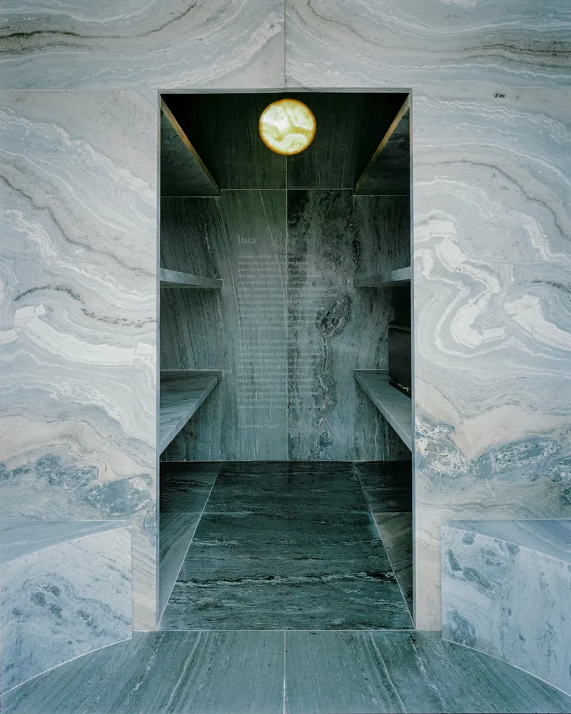 View through a doorway into a vaulted interior lined with veined grey marble and a suspended circular light fixture