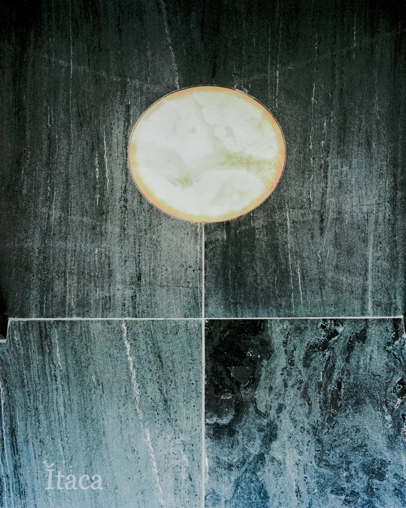 Detail of a backlit translucent stone disc with brass edging against dark veined marble wall panels