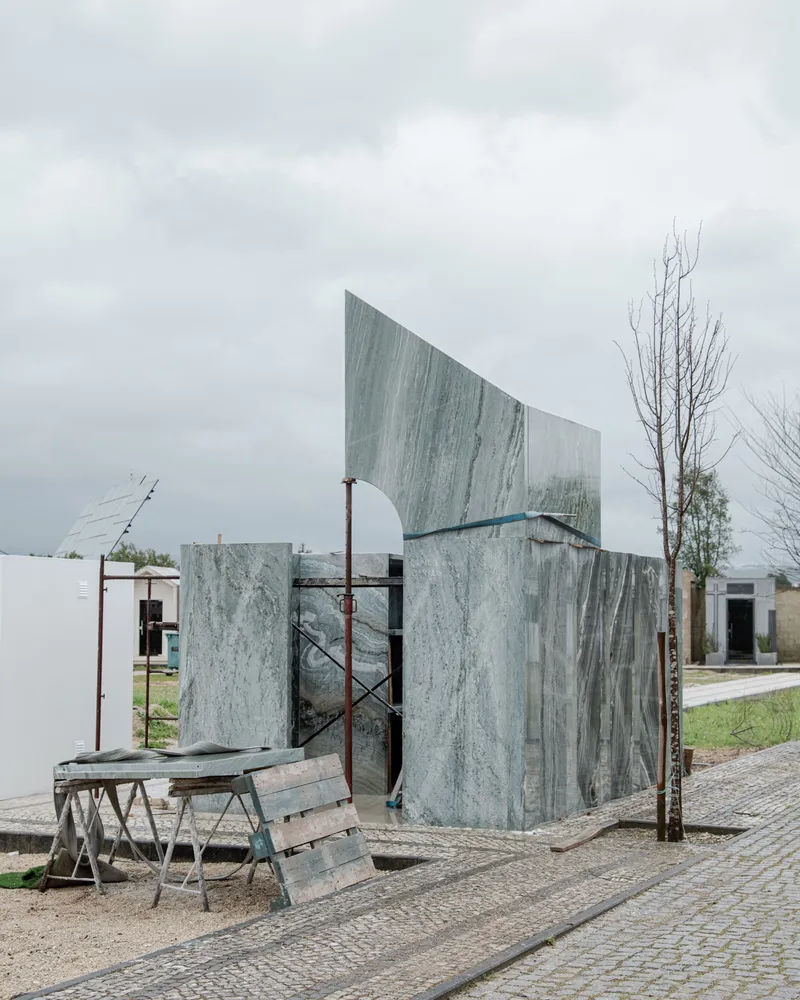 Curving volumetric facade clad in veined grey marble panels under construction on a cloudy day
