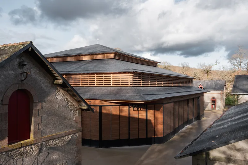 Elevated view of the timber-clad volume with horizontal slat screens and multi-level slate roof under dramatic clouds