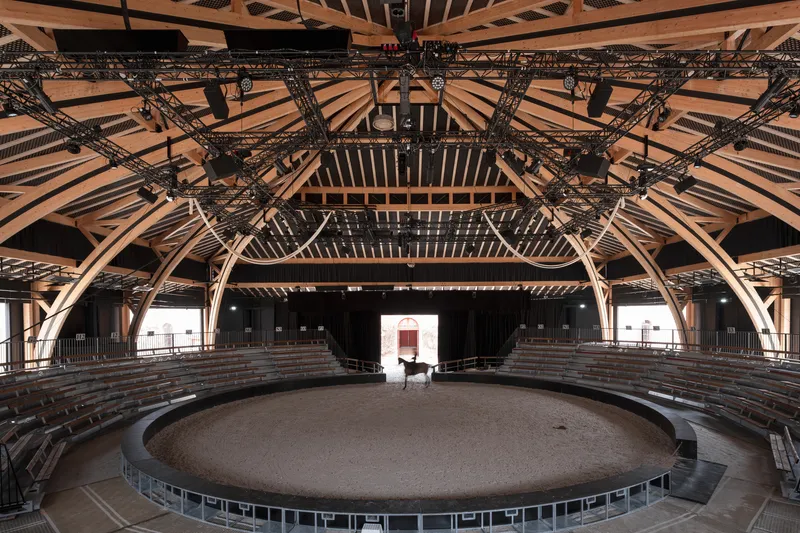 Interior of the circular arena with exposed timber rafters, steel trusses, and tiered seating under clerestory roof