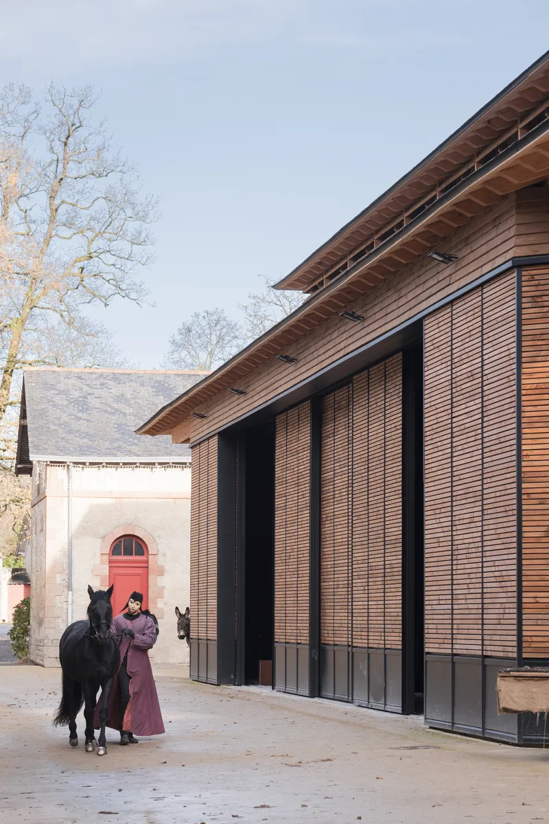 Corner of the timber structure with sloping roof and handler with horse beside the entrance