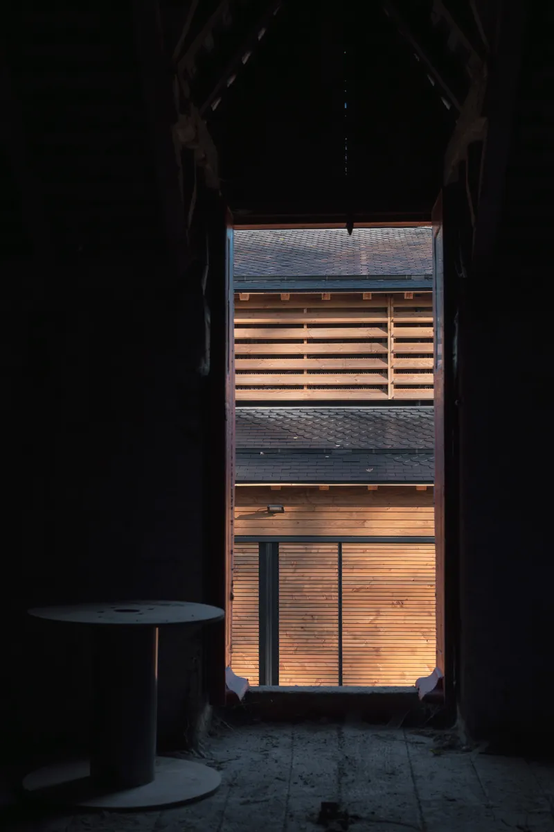 View through a darkened archway toward the backlit timber slatted facade at dusk