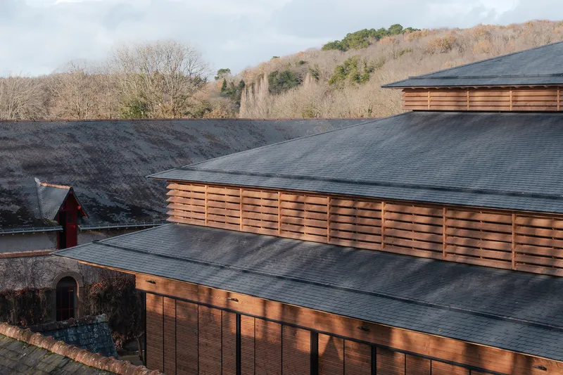 Layered rooflines with dark tiles and timber louvered screens against winter hillside