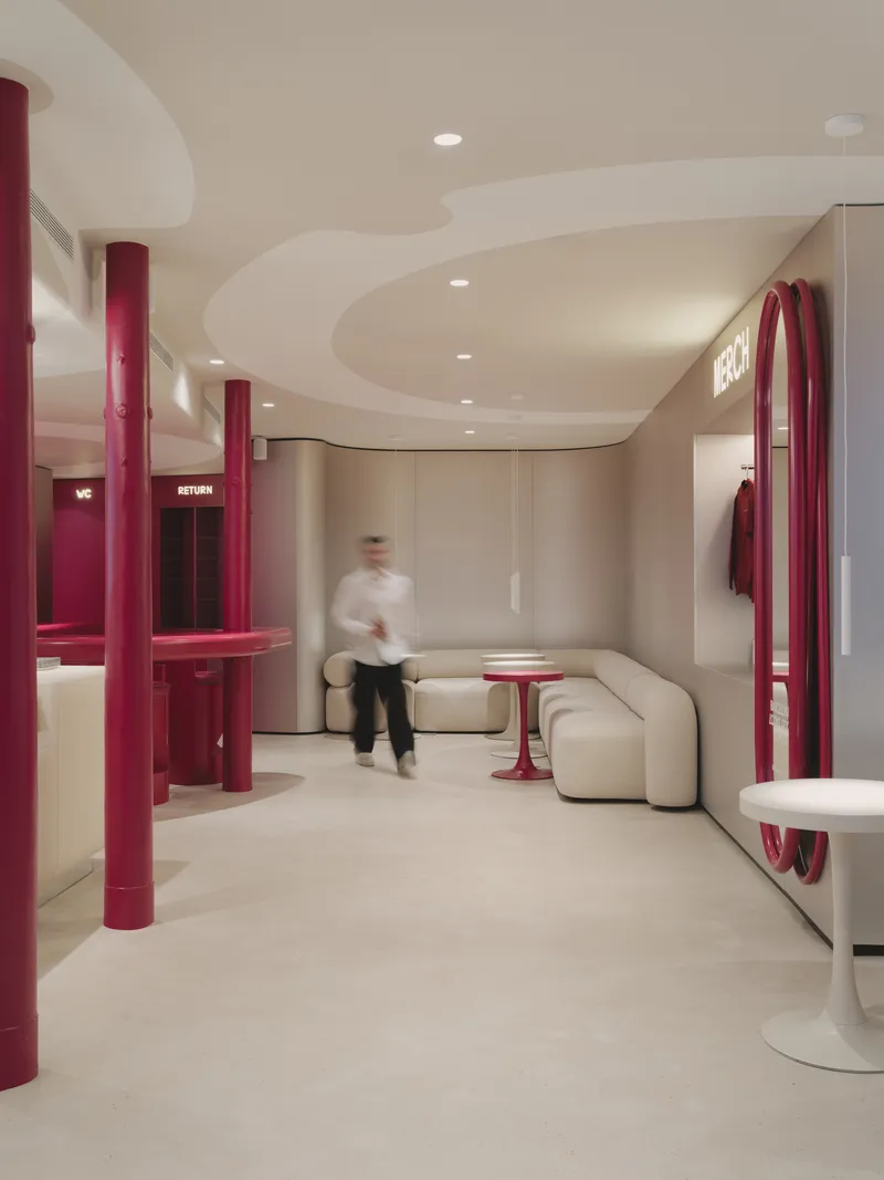 Interior corridor with person in motion passing between burgundy columns and cream modular seating