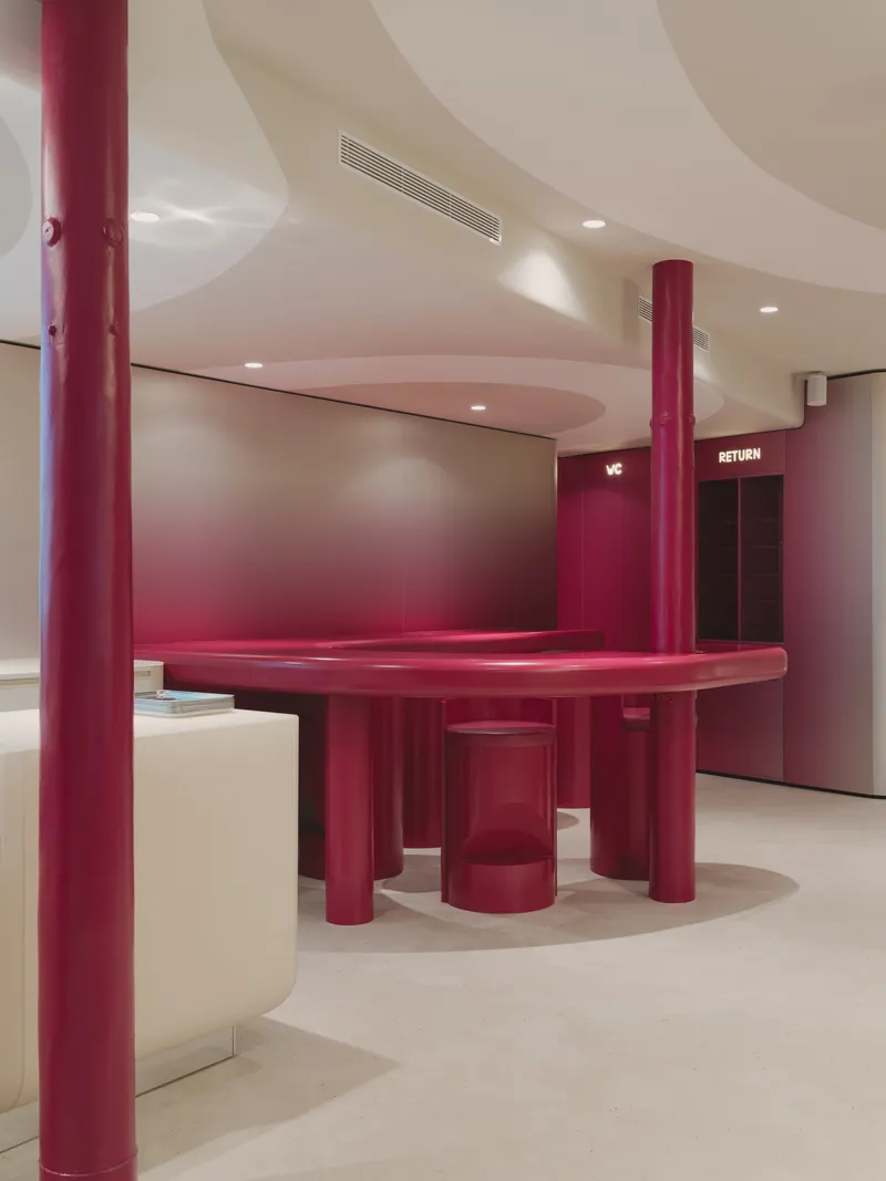 Glossy magenta table with cylindrical stools beneath curved ceiling coffers and recessed lighting