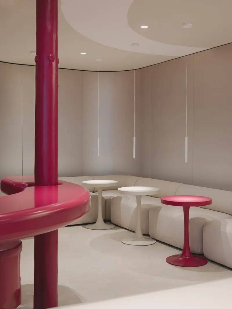 Curved wall of beige panels with white pendant lights above modular seating and pedestal tables