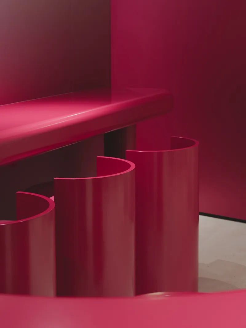 Close-up of three cylindrical magenta stools tucked beneath a glossy counter in dim light