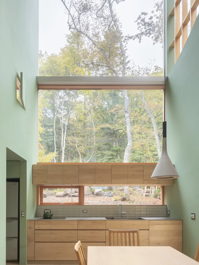 Kitchen with stacked windows framing birch trees and timber cabinetry beneath mint green walls