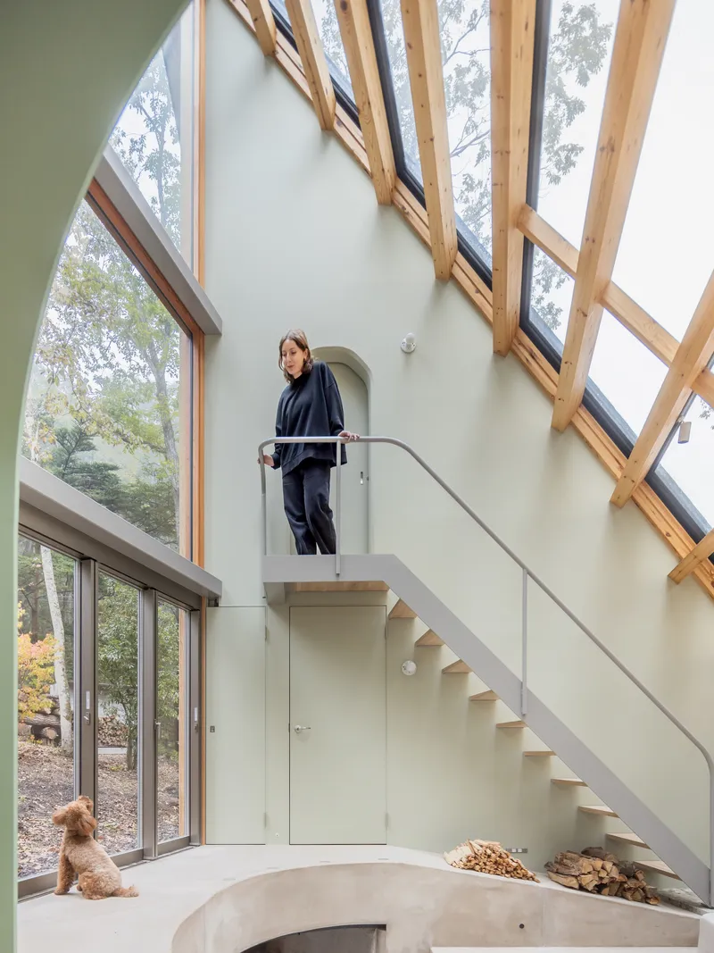 Open staircase with glass railing beneath angled skylights and timber frame with a person ascending