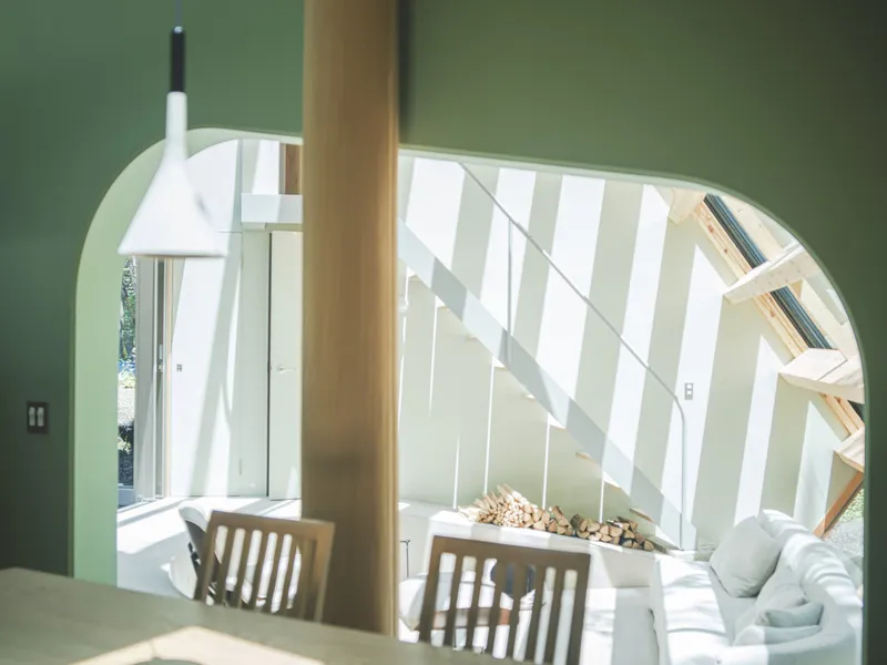 Arched opening framing a dining table and living area with striped sunlight across pale walls