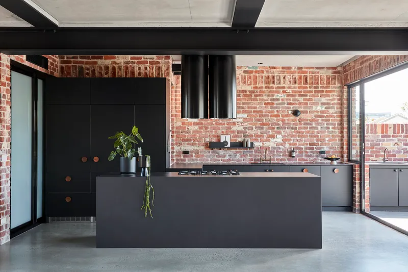 Black matte kitchen island beneath exposed brick walls and a cylindrical range hood