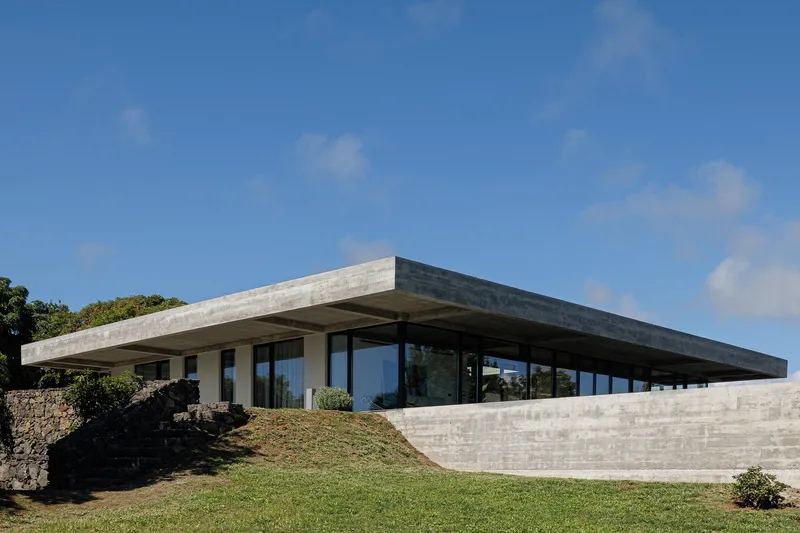 Cantilevered concrete roof plane extending over a glass-walled volume set into a grassy slope