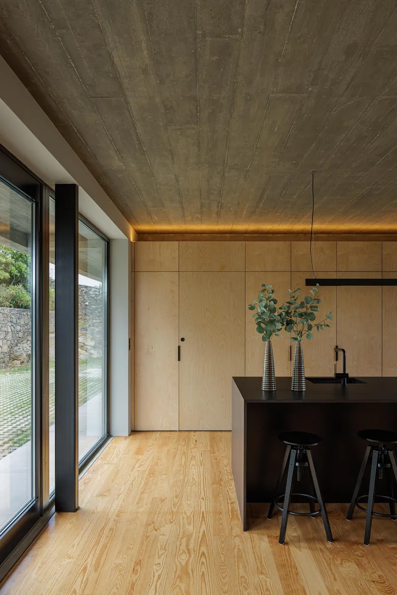 Kitchen with black island under board-formed concrete ceiling and concealed linear lighting at the perimeter