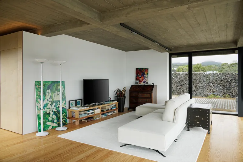 Living area with board-formed concrete ceiling and full-height glazing opening onto a paved courtyard