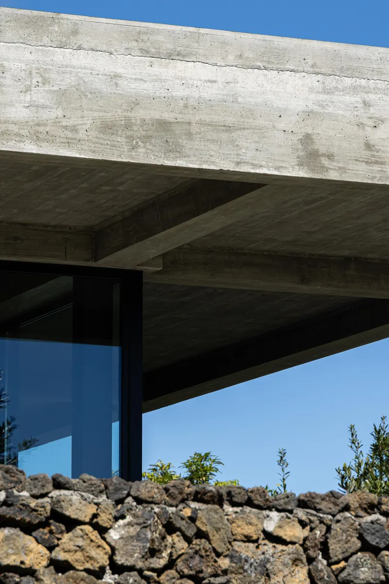 Detail of concrete roof structure showing intersecting beams with board-formed texture against blue sky