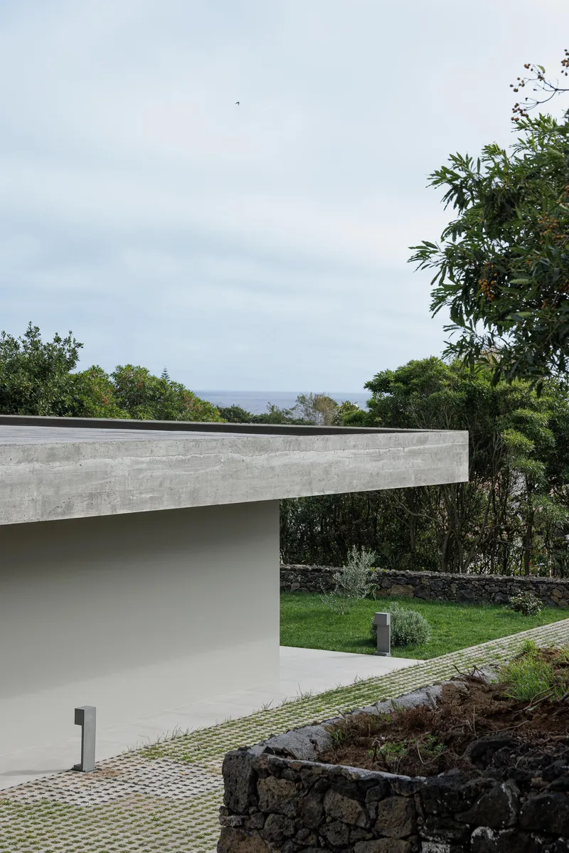 Concrete roof edge projecting over terraced garden with ocean horizon visible through distant vegetation