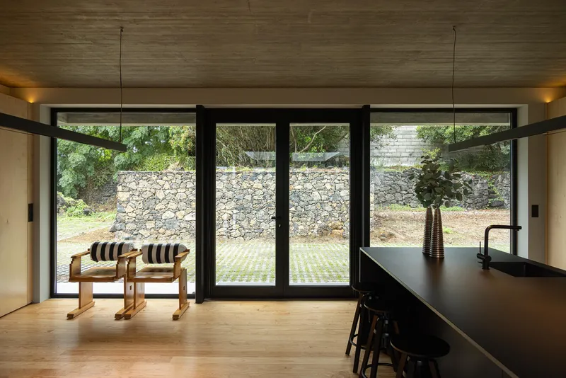 Interior view through black-framed glass doors to a terraced stone retaining wall and garden beyond