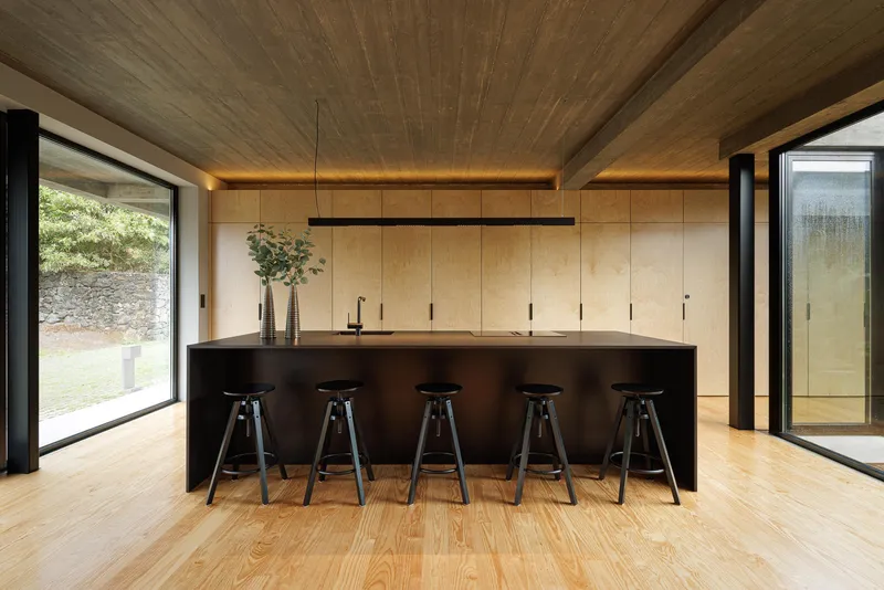 Kitchen island with black metal countertop and five bar stools beneath a wooden plank ceiling