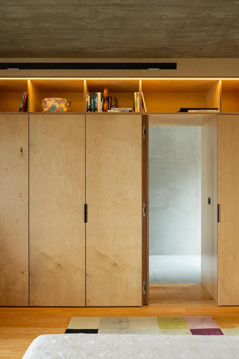 Sliding plywood door opening to reveal an illuminated shelf above built-in storage panels