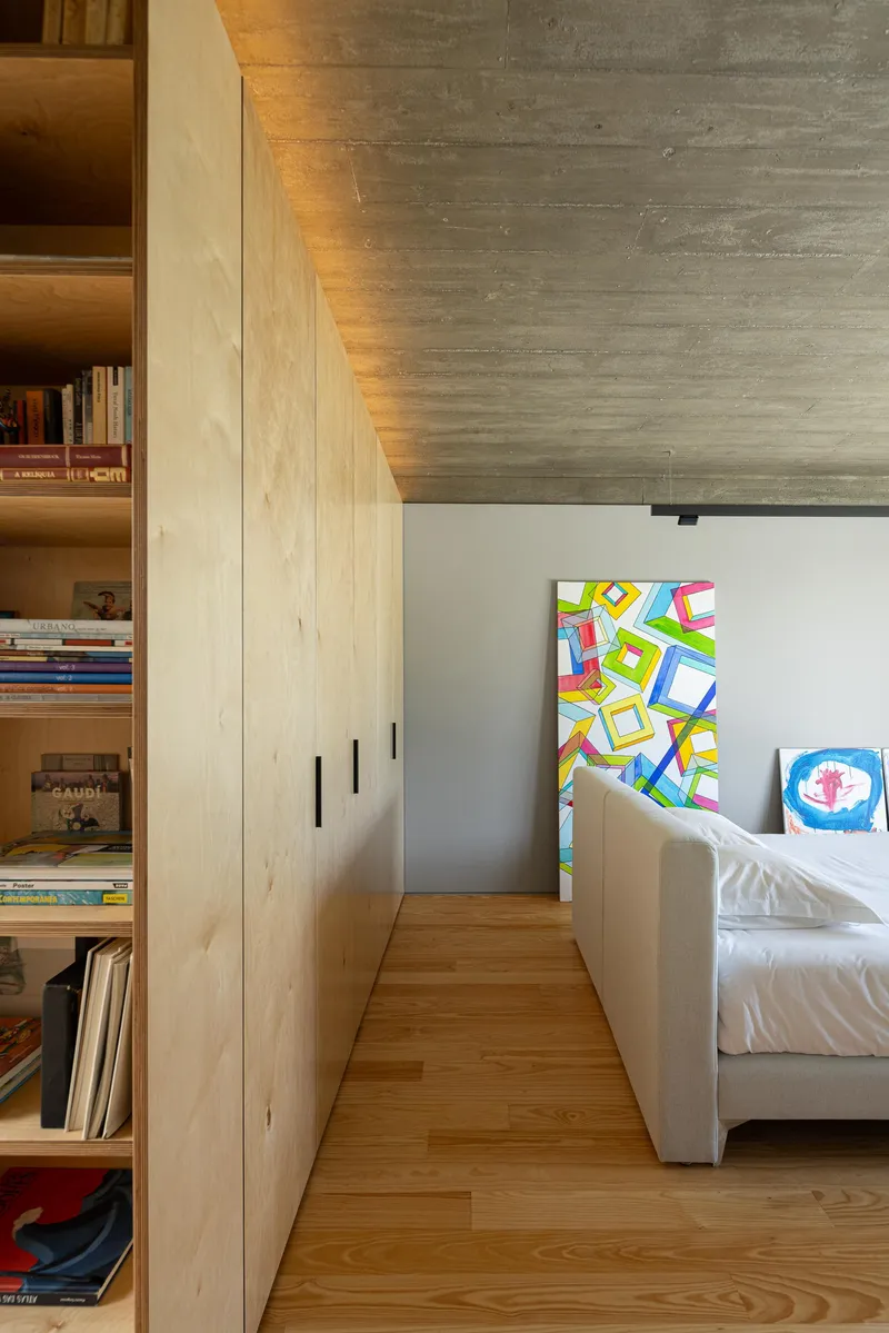 Plywood storage wall with exposed shelving and colorful artwork leaning against white partition