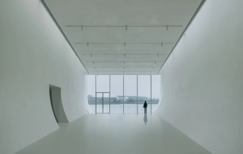 Gallery space with curved white walls and full-height glazing overlooking a misty waterfront