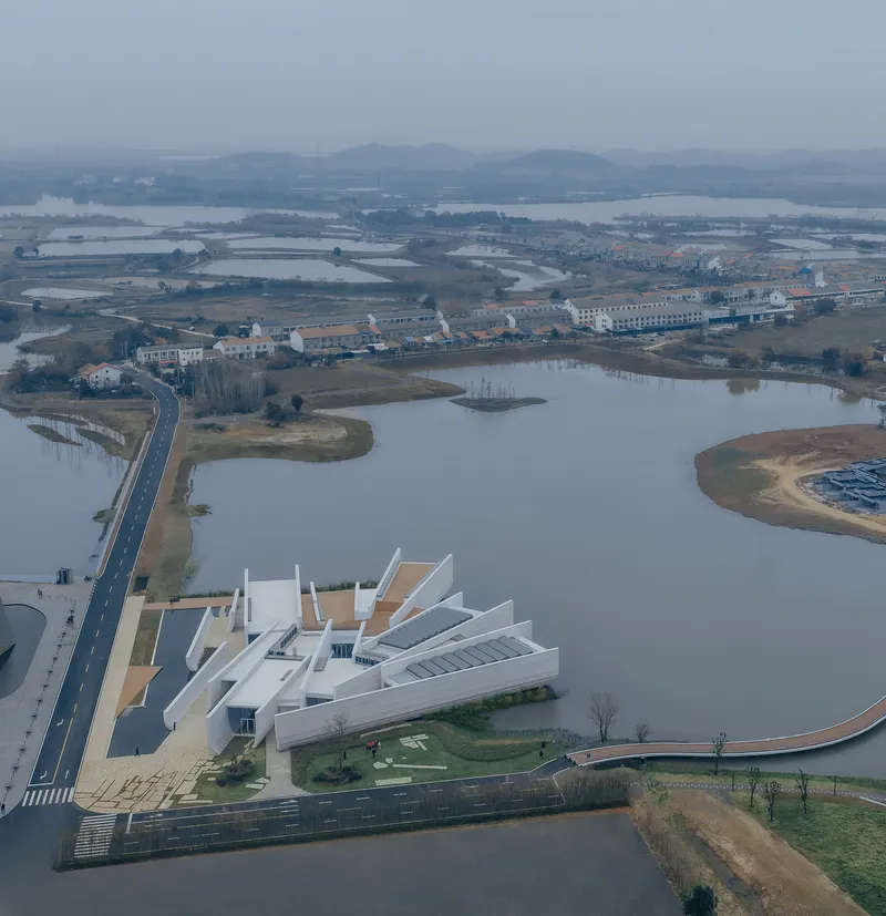 Aerial view of the white multi-winged complex alongside a river and wetlands under hazy sky