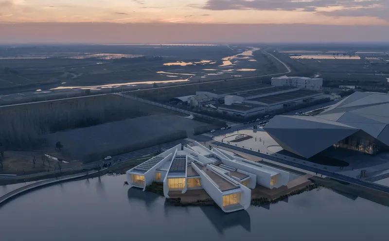 Aerial view of white clustered pavilions with illuminated interiors beside wetlands at dusk