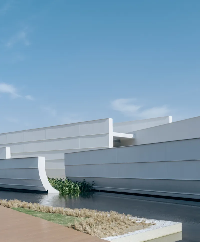 White horizontal panel facade with curved relief adjacent to a water feature and planted grasses