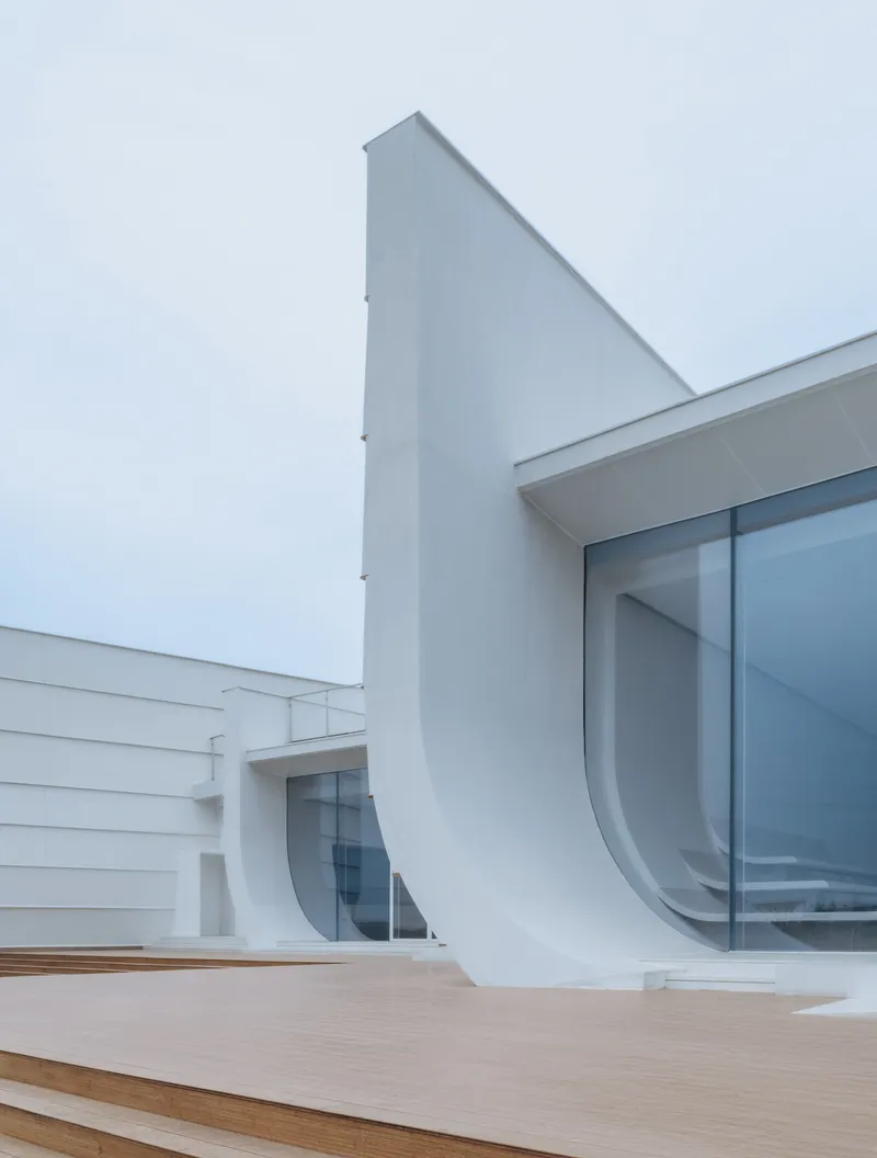 Close-up of the curved white facade element meeting floor-to-ceiling glazing and timber decking
