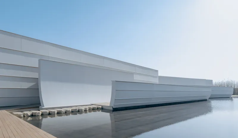 Long view of the layered white facade extending over still water under overcast skies