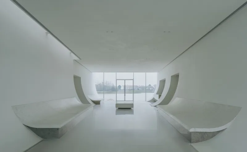 Symmetrical gallery space with paired curved benches flanking glazed wall opening to water view