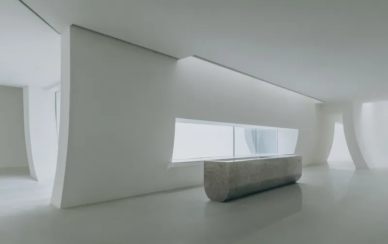 Reception desk in grey concrete beneath a horizontal window framed by curved white walls
