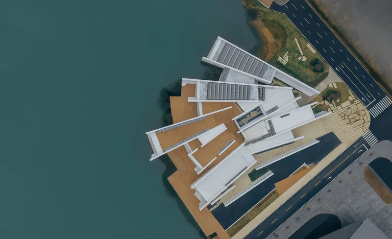 Aerial view of white angular volumes with timber decking extending over teal water