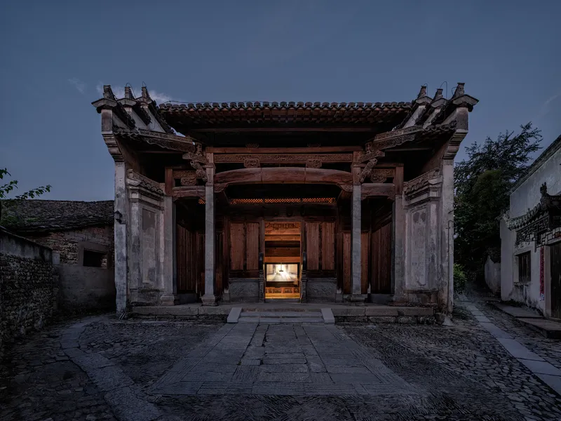 Front elevation of a timber-framed pavilion with carved brackets and tiled roof at dusk