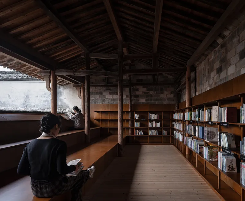 Reading room interior with low bookshelves, exposed timber roof structure and two visitors at desks