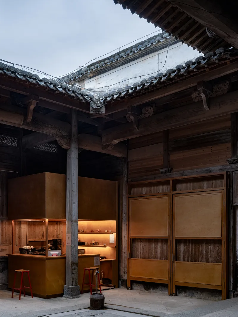 Interior courtyard with illuminated service counter and timber columns beneath traditional tiled roof overhang at dusk