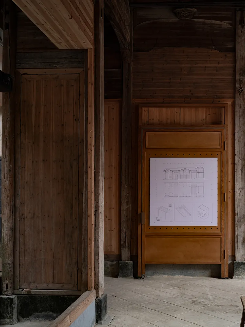 Technical drawings of elevations and plans displayed in timber-framed panel against wood-clad interior wall