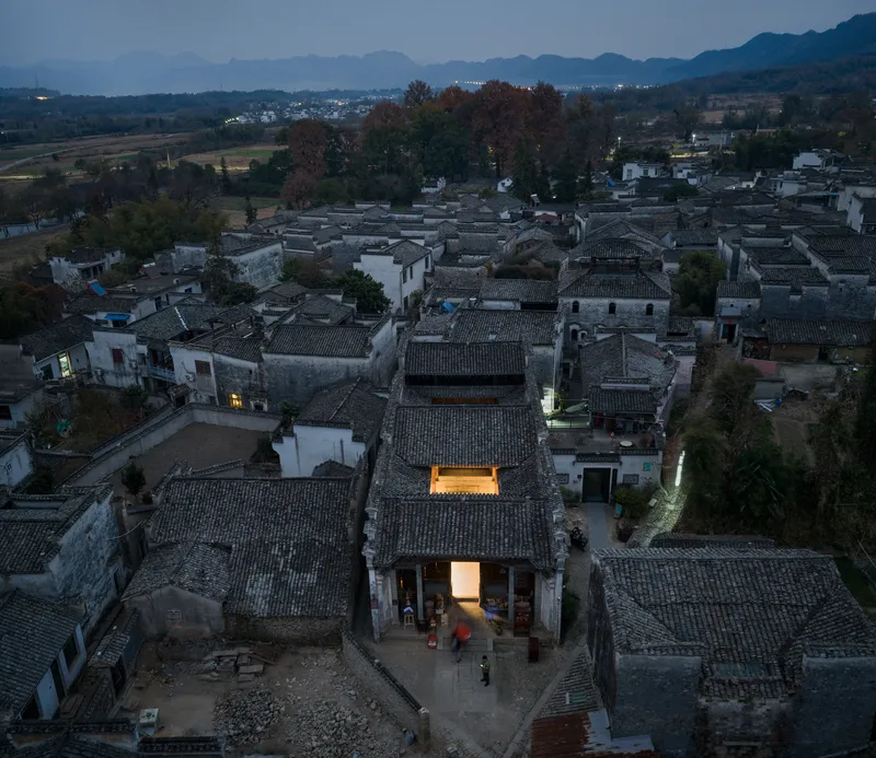 Aerial view of tiled rooftops at dusk with illuminated courtyard and distant mountains