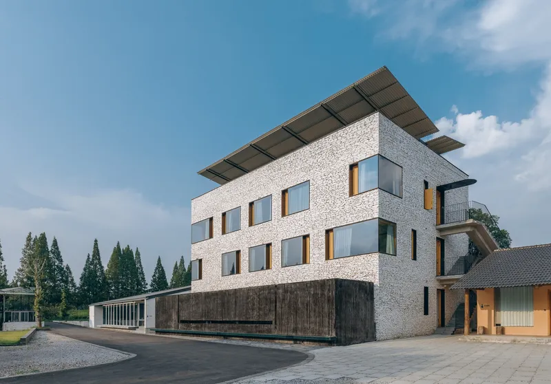 Three-story volume with white terrazzo facade, dark timber base, and solar panel canopy under blue sky