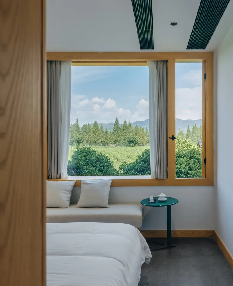 Bedroom with timber-framed window seat overlooking tea plantation and distant mountains on a partly cloudy day