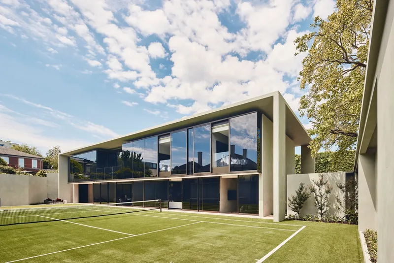 Rear elevation with floor-to-ceiling glazing overlooking a tennis court with synthetic grass surface