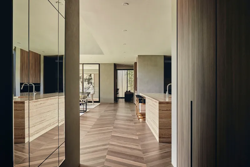 View through doorway into kitchen with chevron timber flooring and concrete wall panels