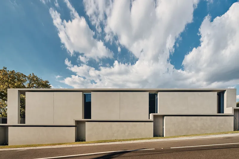 Street view of the rectilinear concrete facade with narrow vertical window slots under scattered clouds